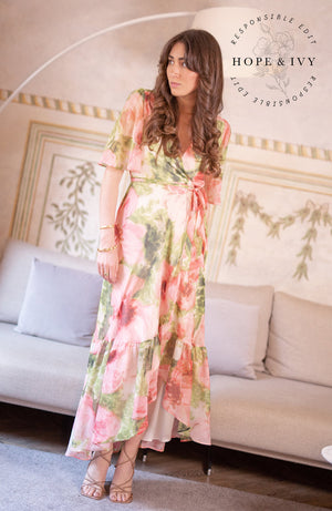 The hand-design print depicts romantic brushed petals in muted florals scattered on a soft base. Full flutter sleeves and a tie waist feature complete the wrap front bodice with a drop hem skirt that finishes at floor length. Whatever this Spring has in hold for you, glide with grace in this celestial dress.