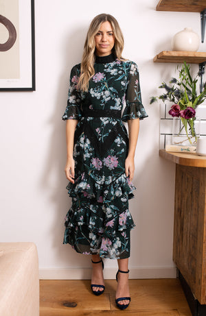 Hand-designed soft florals brush the green base in soft blues and pinks. The high cut neckline boasts statement lace trim that also covers the waist and skirt. Style down with ankle boots for day-to-day looks, or style up with heels for dressy occa