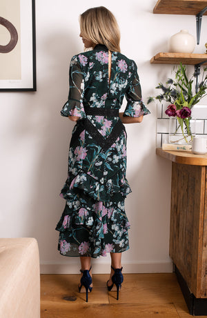Hand-designed soft florals brush the green base in soft blues and pinks. The high cut neckline boasts statement lace trim that also covers the waist and skirt. Style down with ankle boots for day-to-day looks, or style up with heels for dressy occa