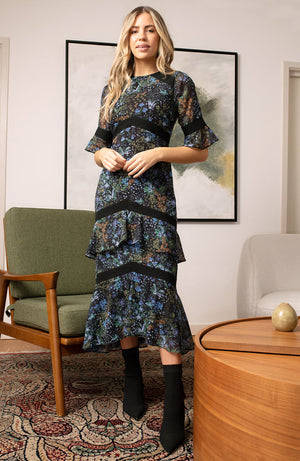 Hand-designed ditsy florals bloom across the dark base in powerful blue, green and orange tones. With tiered skirt and bell sleeves, this figure hugging pencil midi style dress is undeniably flattering. Finished with lace trims, dress up or down for the perfect transitional piece this Autumn.