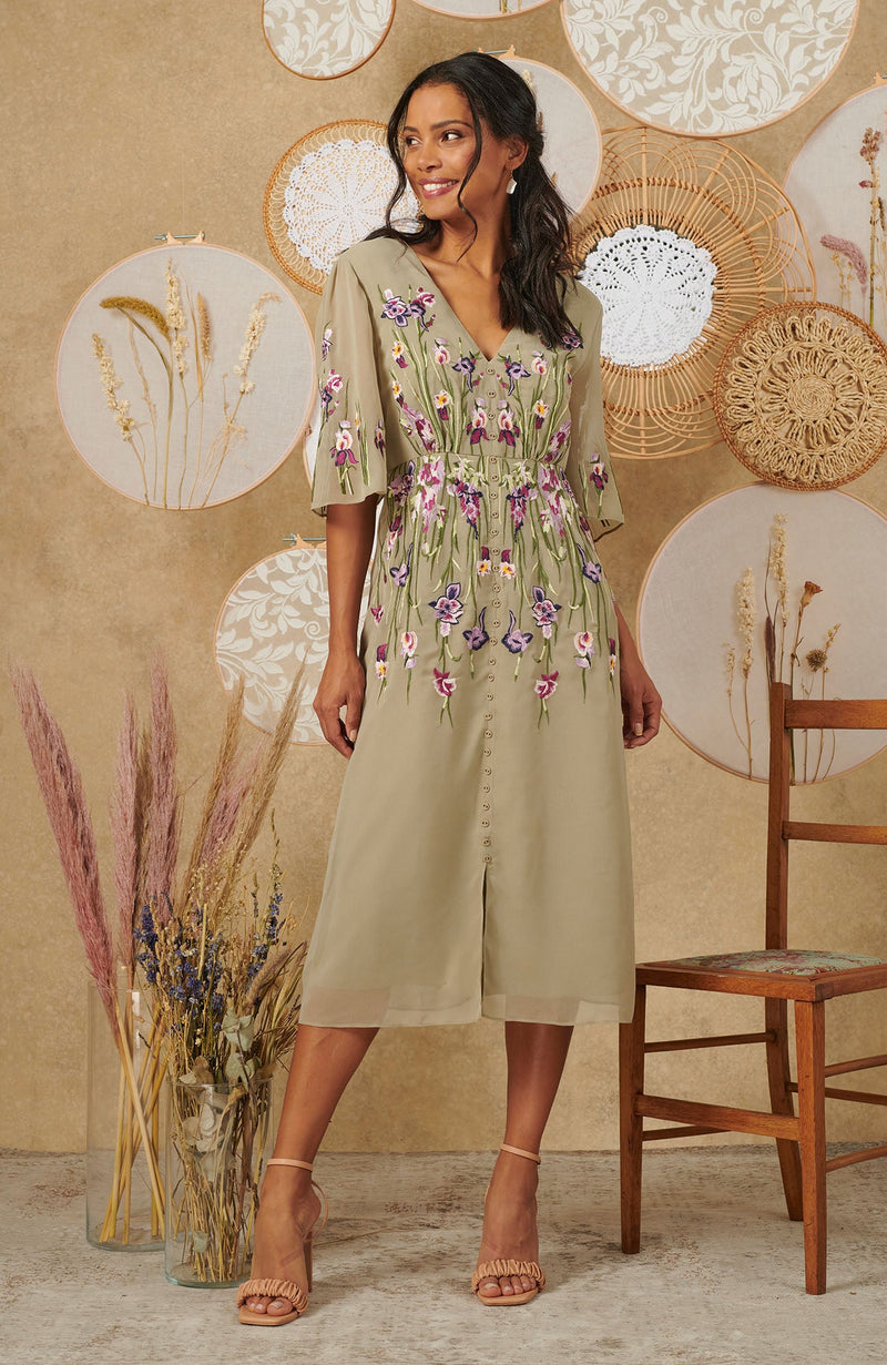 The soft Sage base is beautifully adorned with a hand-finished floral embroidery, on the bust, shoulder and skirt. Featuring a v-neckline and romantic flutter sleeve, the piece is further elevated by the button front detailing. The skirt front split allows for ease of wear, flowing down to finish at calf length.