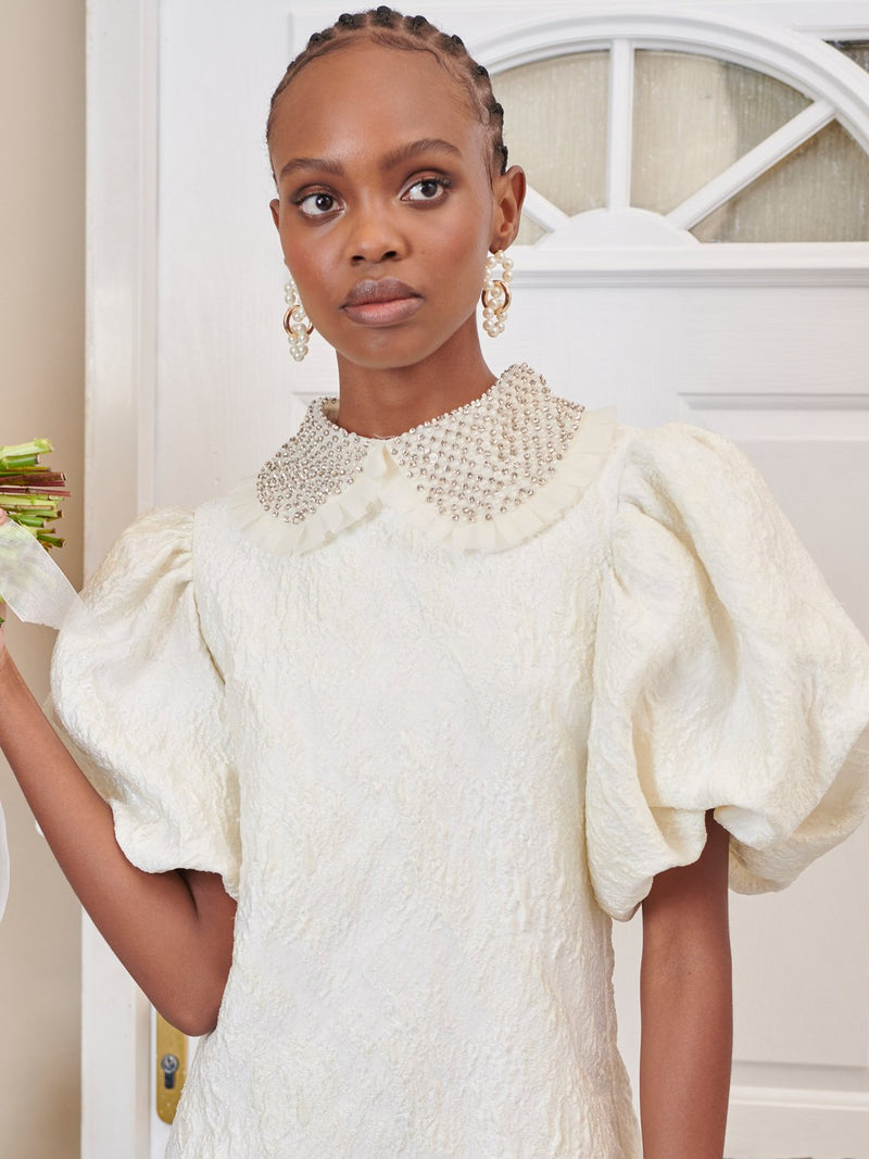 Dream Sister Jane Papier embellished ivory mini dress in a textured jacquard fabric. Detailed with a gem embellished collar and puff sleeves. This style is fully lined in a soft touch fabric.