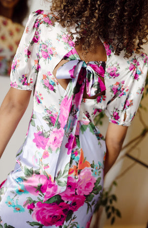 Contrasting panels of hand-designed stylised florals bloom across lilac and white satin bases, in power pinks and oranges. With a puff blouson sleeve, tie back detail and high cut neckline, this gorgeous silhouette is sure to inspire and enchant onlookers whatever the event this season.