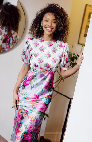 Contrasting panels of hand-designed stylised florals bloom across lilac and white satin bases, in power pinks and oranges. With a puff blouson sleeve, tie back detail and high cut neckline, this gorgeous silhouette is sure to inspire and enchant onlookers whatever the event this season.