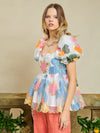 Sister Jane DREAM Primula Postcard Scallop Top. Open back top in a bright floral organza jacquard fabric. Featuring a scallop edge neckline and hem with short puff sleeves. Adjustable ties bow at the back. Fully lined in a soft touch fabric