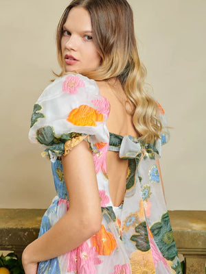 Sister Jane DREAM Primula Postcard Scallop Top. Open back top in a bright floral organza jacquard fabric. Featuring a scallop edge neckline and hem with short puff sleeves. Adjustable ties bow at the back. Fully lined in a soft touch fabric
