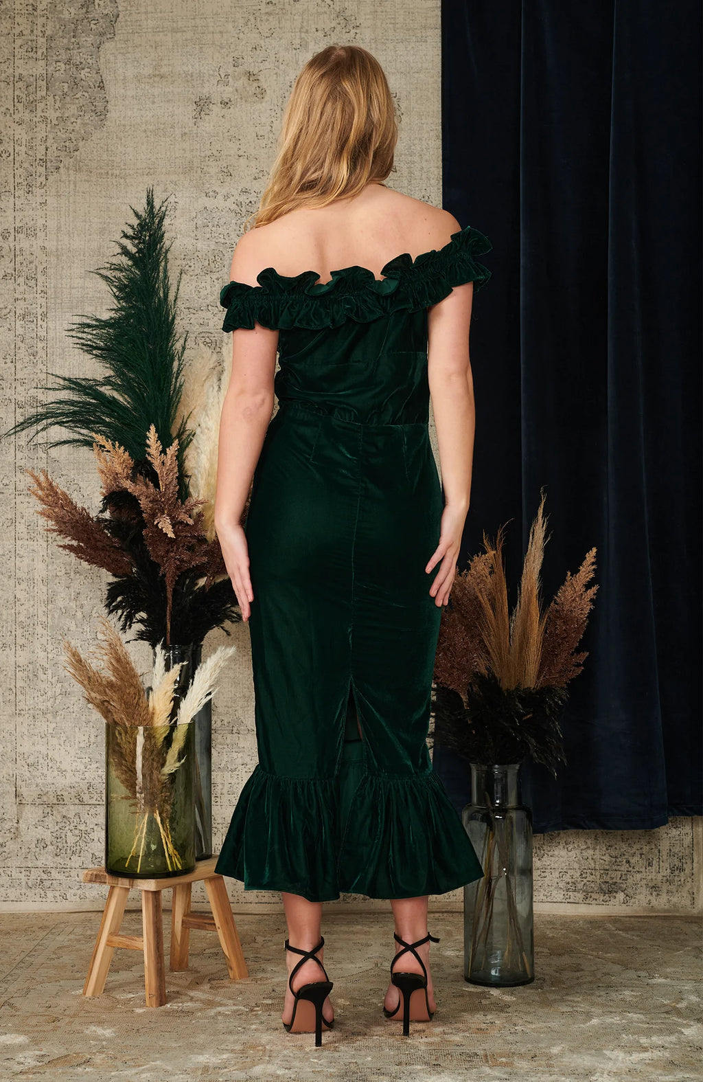 The bardot neckline is trimmed with an exaggerated ruffle for standout impact, and the figure skimming pencil skirt cuts a flattering silhouette. The rich dark green velvet both looks and feels lovely, and is perfect for any party or event this season.