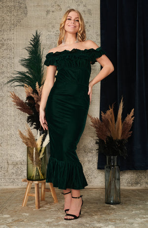 The bardot neckline is trimmed with an exaggerated ruffle for standout impact, and the figure skimming pencil skirt cuts a flattering silhouette. The rich dark green velvet both looks and feels lovely, and is perfect for any party or event this season.